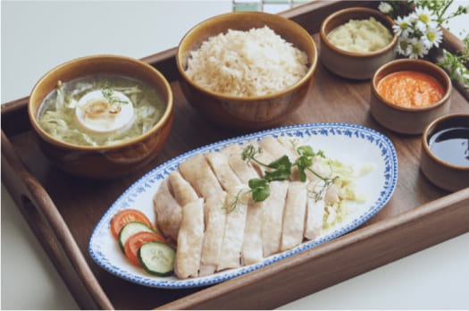 Sliced chicken on a plate with rice, soup, sauces, and a garnish served on a wooden tray, suggesting a meal ready to be eaten.