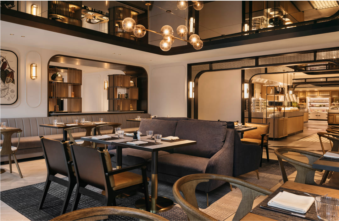 Elegant dining area with tables set for service, featuring modern lighting and a visible second-floor balcony, forming a sophisticated restaurant interior.