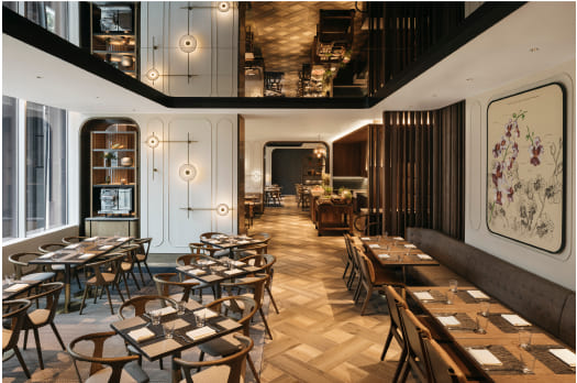 An elegant restaurant with wooden tables and chairs, herringbone flooring, and modern décor, illuminated by ambient lighting, creating a cozy dining atmosphere.