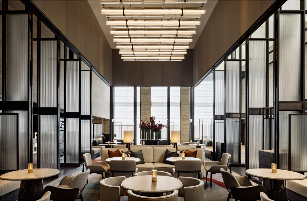 Modern lounge area with sofas and tables, ambient lighting, framed by geometric room dividers and expansive windows. The space conveys an upscale, contemporary interior.