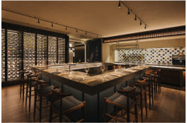 A modern bar with stools around a central counter; wall-mounted wine racks and decorative tiles in the background create an upscale ambiance. No text is present.