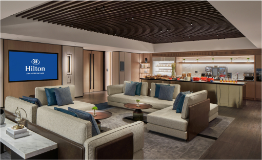 A modern meeting space with arranged chairs around a central table, facing two screens displaying the 'Hilton' logo. The context is an indoor corporate setting.